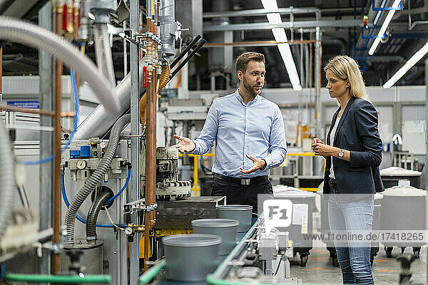 Male professional explaining over machine to female manager in factory