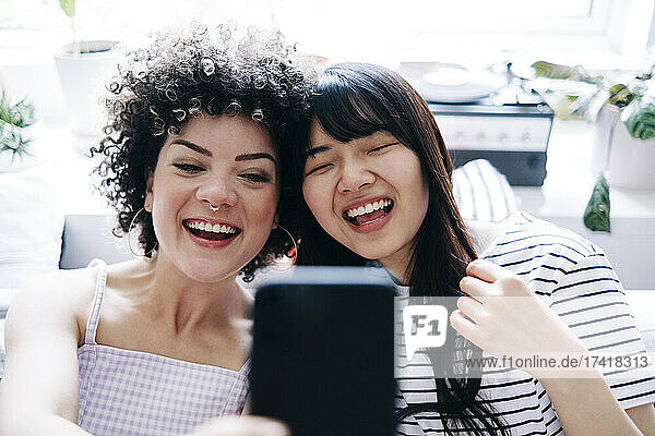 Cheerful female friends taking selfie through smart phone at home