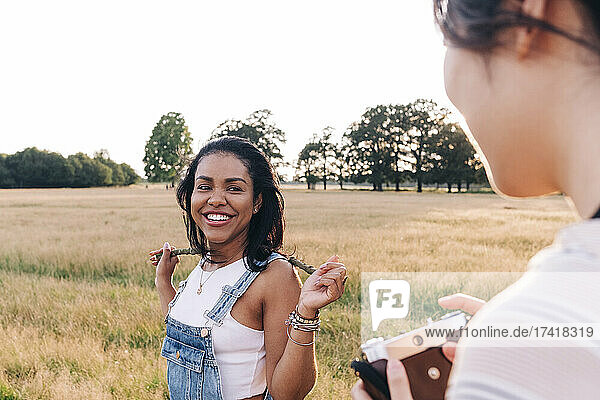 Smiling woman holding stick while looking at friend with camera