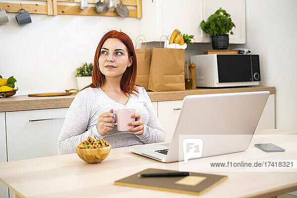 Thoughtful woman with coffee mug looking away while sitting at home office