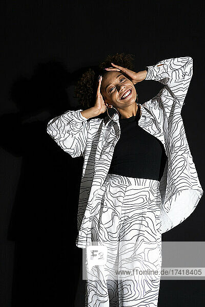 Smiling trendy woman with head in hands against black background