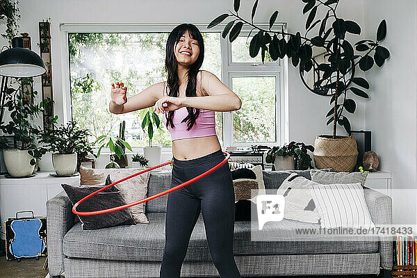 Lächelnde Frau trainiert mit Plastikreifen im Wohnzimmer