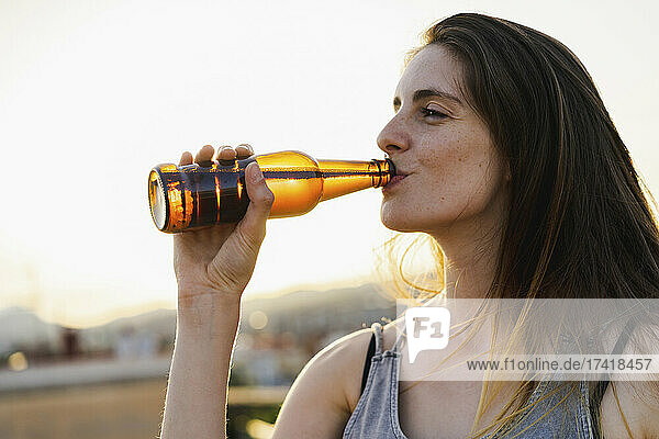 Woman drinking beer at rooftop during sunset