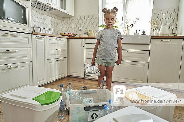 Girl with bunch of newspapers collecting garbage for recycling in kitchen