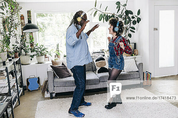 Verspielter Vater und Tochter mit Kopfhörern tanzen zu Hause