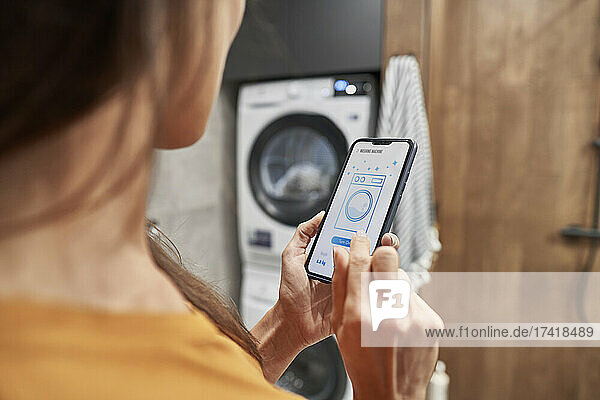 Woman operating washing machine through mobile application at home