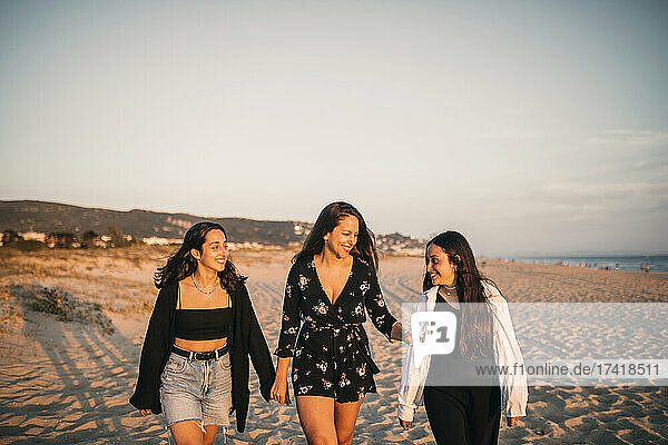 Smiling mother and daughters walking at beach during sunset