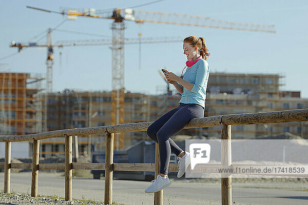 Frau benutzt Mobiltelefon  während sie auf Geländer sitzt