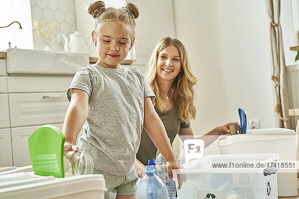 Girl separating garbage with mother in kitchen