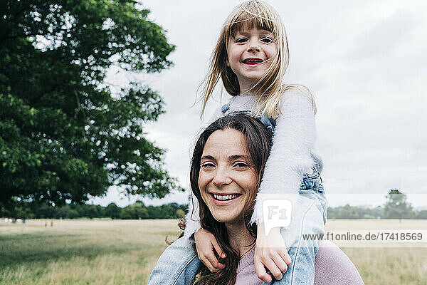 Smiling daughter sitting on woman's shoulders at meadow