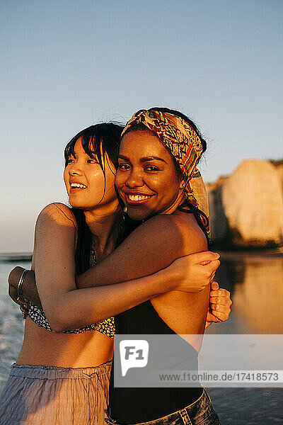 Smiling female friends embracing at beach