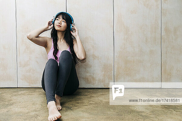 Young woman listening music through headphones while sitting on floor