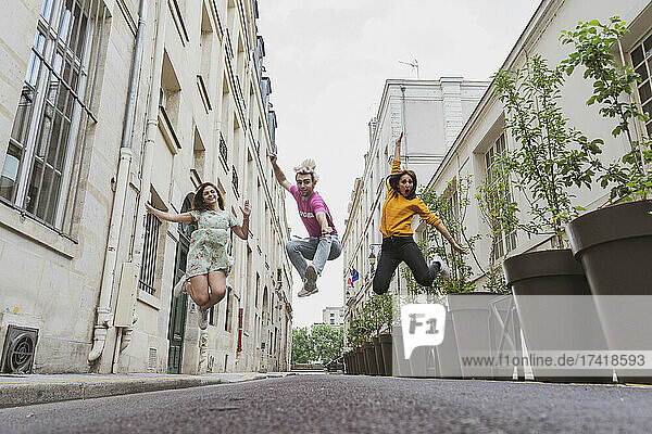 Cheerful male and female friends jumping on street