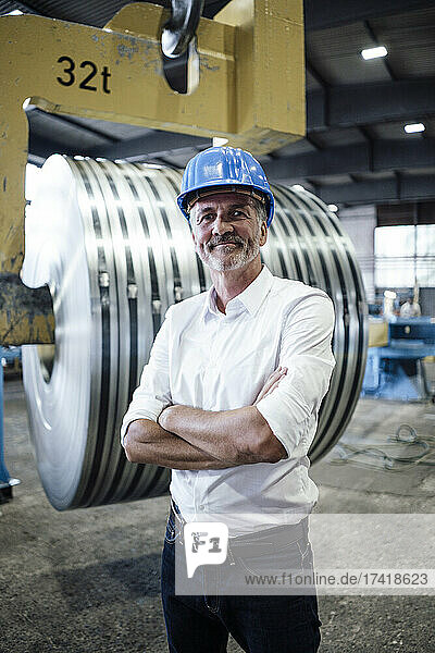 Smiling male professional with arms crossed standing in steel mill