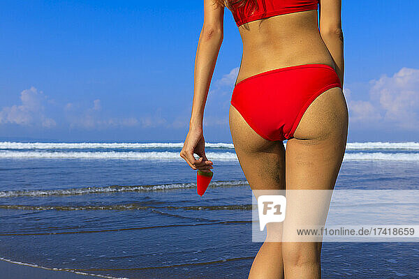 Woman in bikini holding ice cream at beach on sunny day