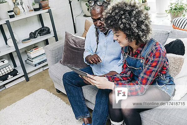 Woman using digital tablet while sitting by father on sofa