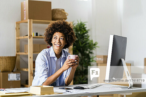 Nachdenkliche Afro-Geschäftsfrau hält Tasse am Schreibtisch im Studio