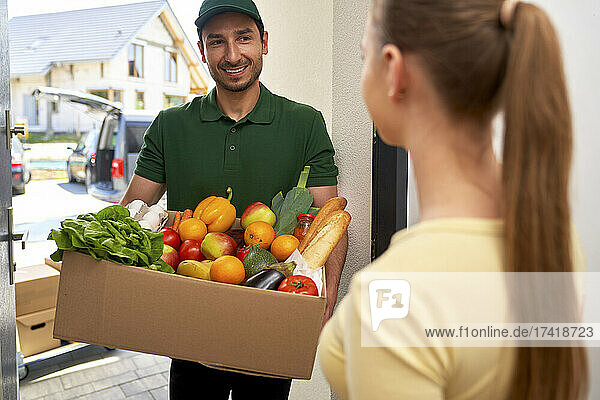 Smiling deliveryman giving grocery order to customer at doorway