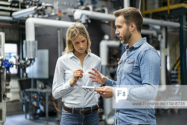 Male professional explaining over equipment to female coworker at industry
