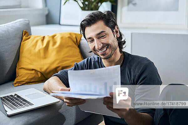 Smiling businessman looking at documents while leaning on sofa at home