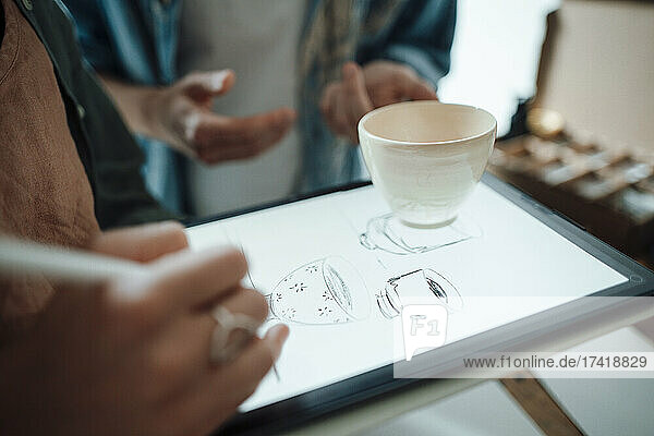 Female artist making cup sketch on graphic tablet while working at home office