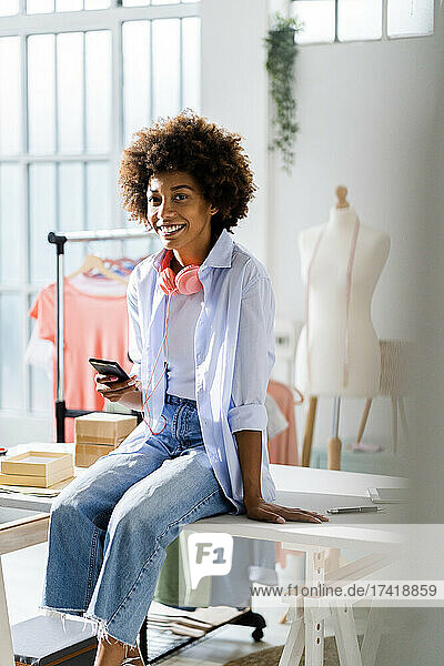 Smiling businesswoman with smart phone sitting on desk at studio