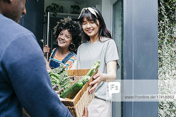 Male delivery person delivering fresh vegetable to women at doorway
