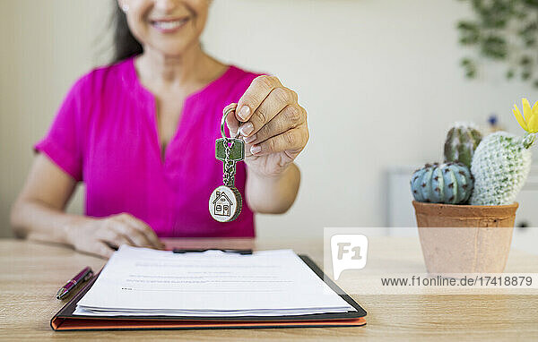 Smiling female real estate agent giving house key at home office
