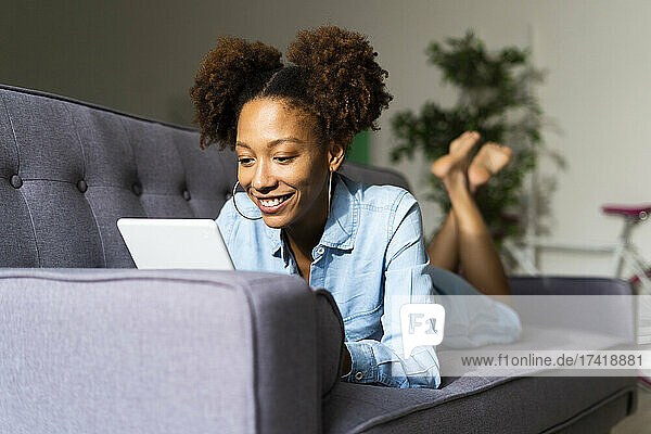 Afro-Frau benutzt digitales Tablet  während sie zu Hause auf dem Sofa liegt