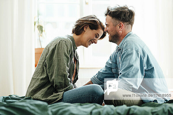 Cheerful mid adult couple sitting on bed at home