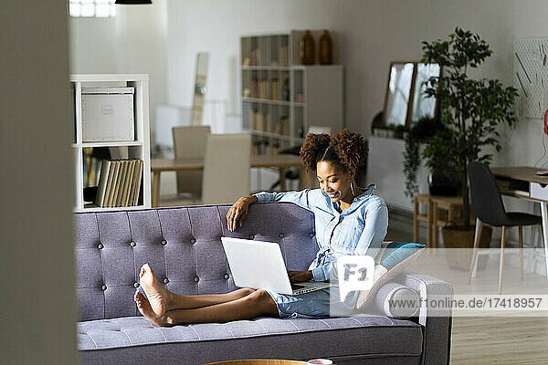 Afro young woman using laptop while sitting on sofa at home