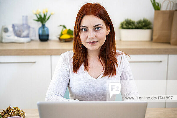 Lächelnde rothaarige Frau mit Laptop zu Hause
