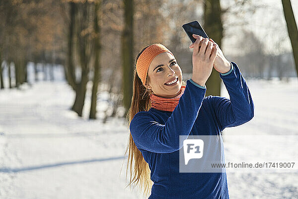 Smiling young woman taking selfie through smart phone during winter