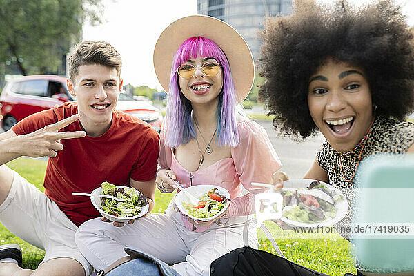 Cheerful woman taking selfie with friends while man showing peace sign