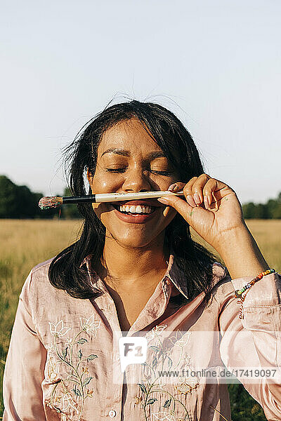 Smiling woman with eyes closed holding paintbrush during sunny day