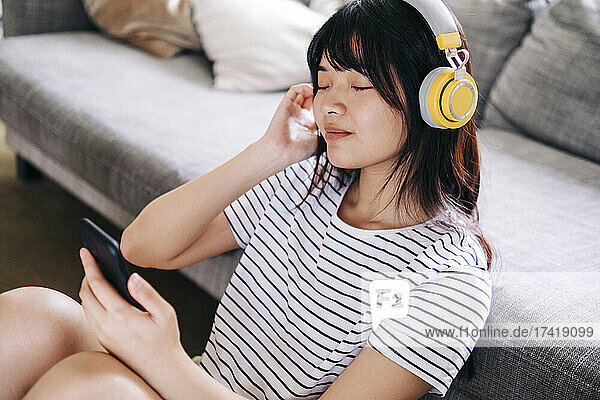 Woman with mobile phone listening music through headphones in living room