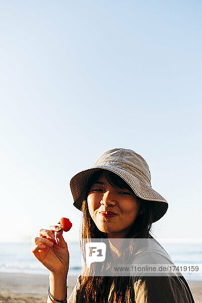 Schöne junge Frau isst Erdbeeren am Strand