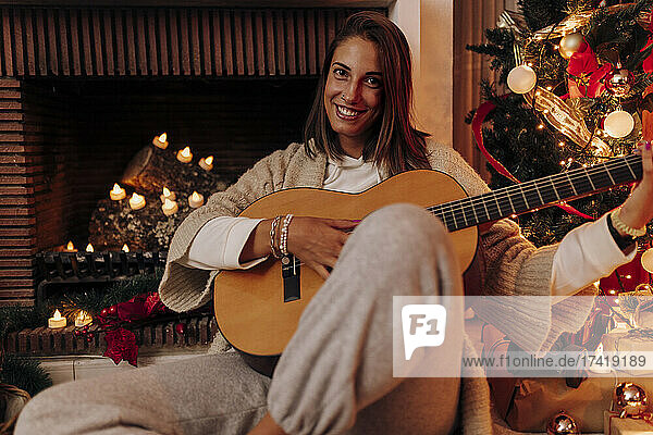 Smiling woman playing guitar while sitting at home during Christmas