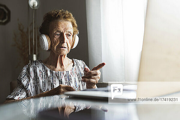 Ältere Frau gestikuliert während Videoanruf über Laptop zu Hause