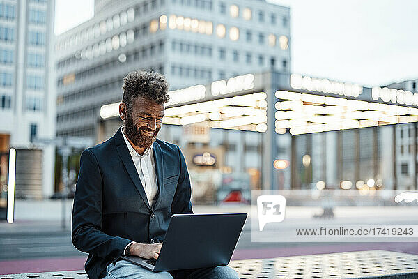 Smiling businessman working on laptop at station