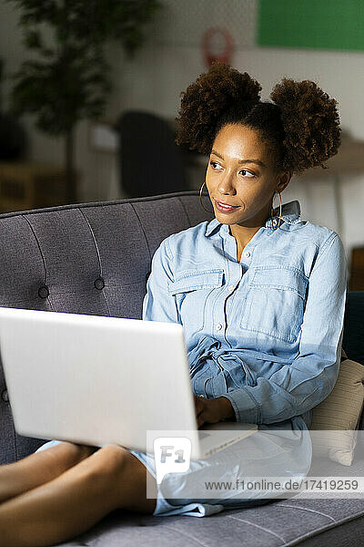 Young woman sitting with laptop on sofa while contemplating in living room