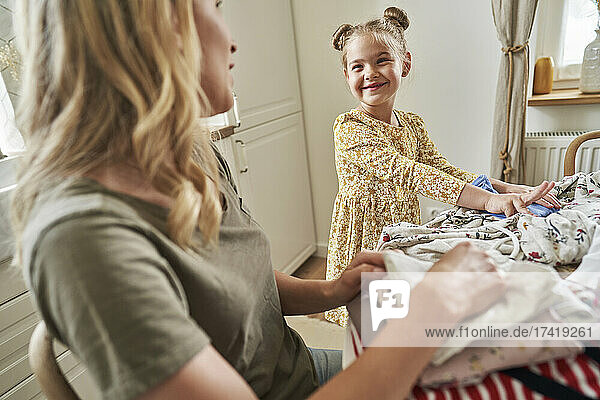 Smiling daughter arranging clothes with mother at home
