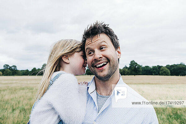Daughter whispering in smiling father's ear at meadow
