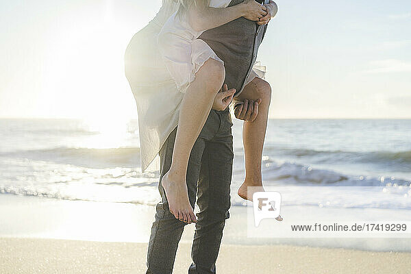 Young groom giving piggyback ride to bride at beach