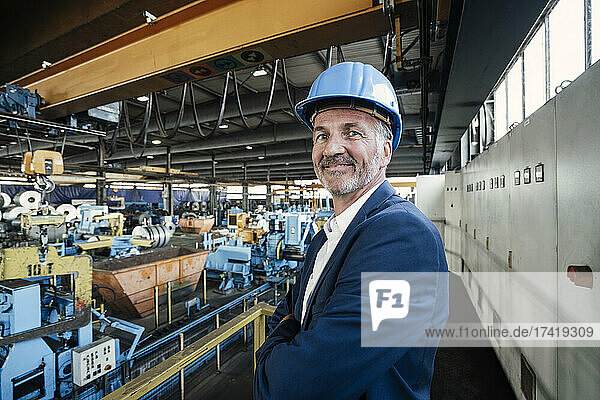 Smiling male engineer with arms crossed standing at steel mill