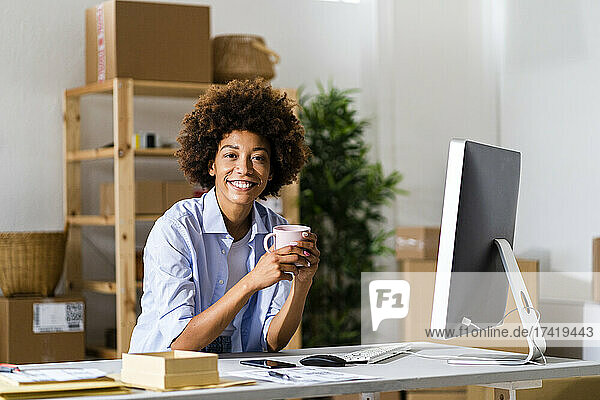 Glückliche junge Geschäftsfrau hält Tasse am Schreibtisch im Studio