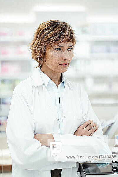 Female pharmacist standing with arms crossed at pharmacy