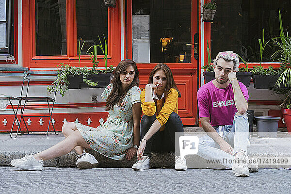 Gay man and female friends sitting together on footpath