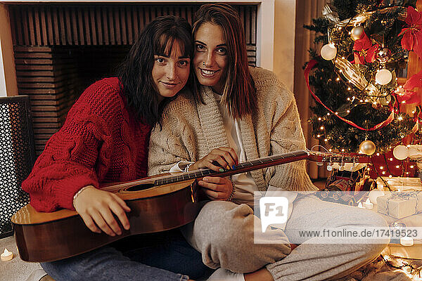 Woman with guitar sitting by female friend at home during Christmas
