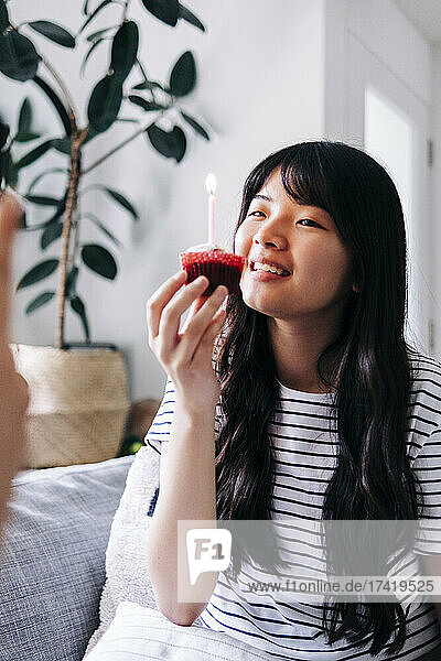 Lächelnde junge Frau hält Cupcake mit Kerze zu Hause